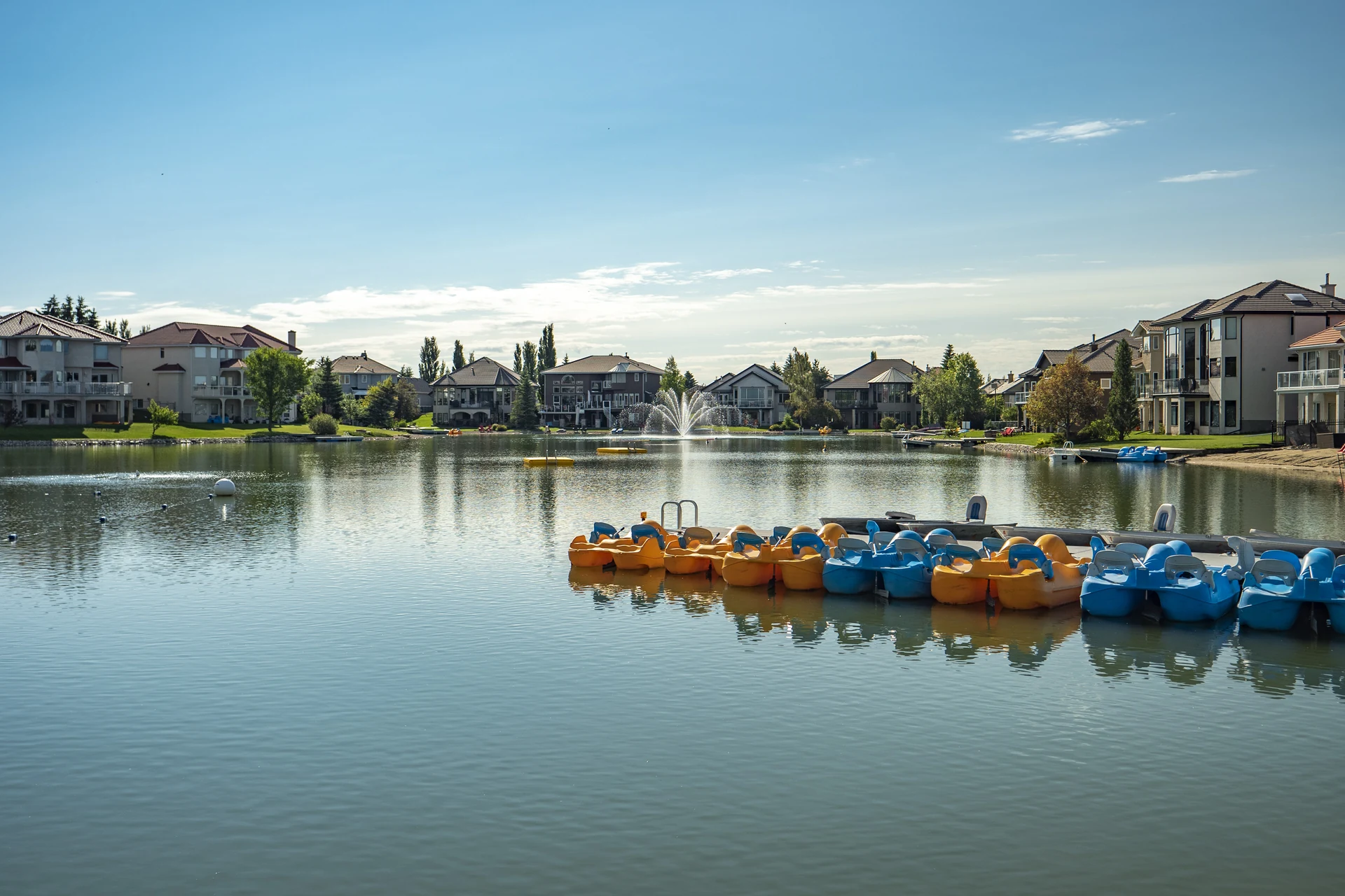 Arbour Lake fountain and waterfront homes beyond a dock lined with orange and blue pedal boats