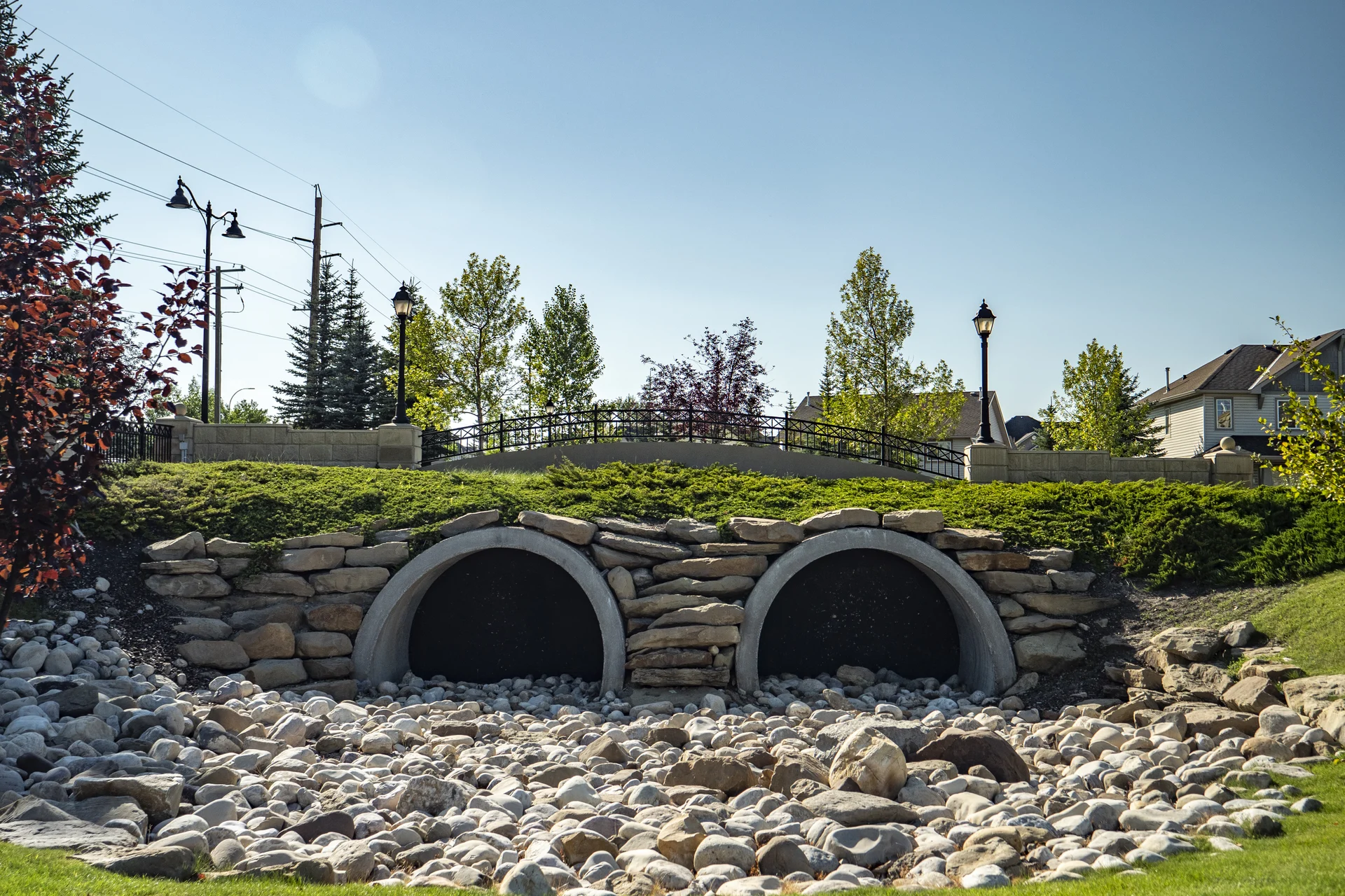 Photograph of Evergreen's twin stone culvert crossing, black railing, lanterns and leafy landscaped paths