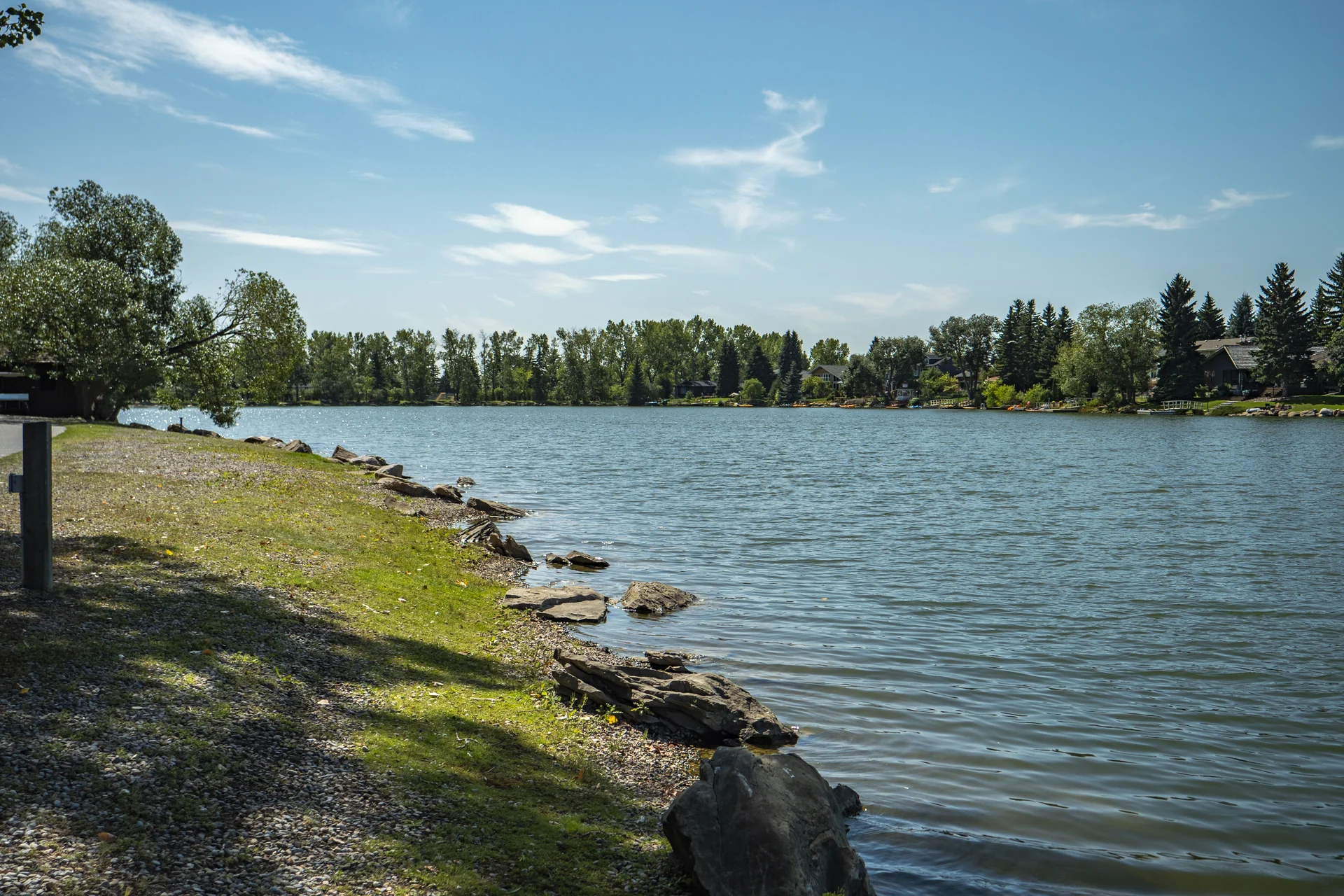 Lake Bonavista from its rocky shoreline, with mature trees, waterfront homes and residential docks across the water