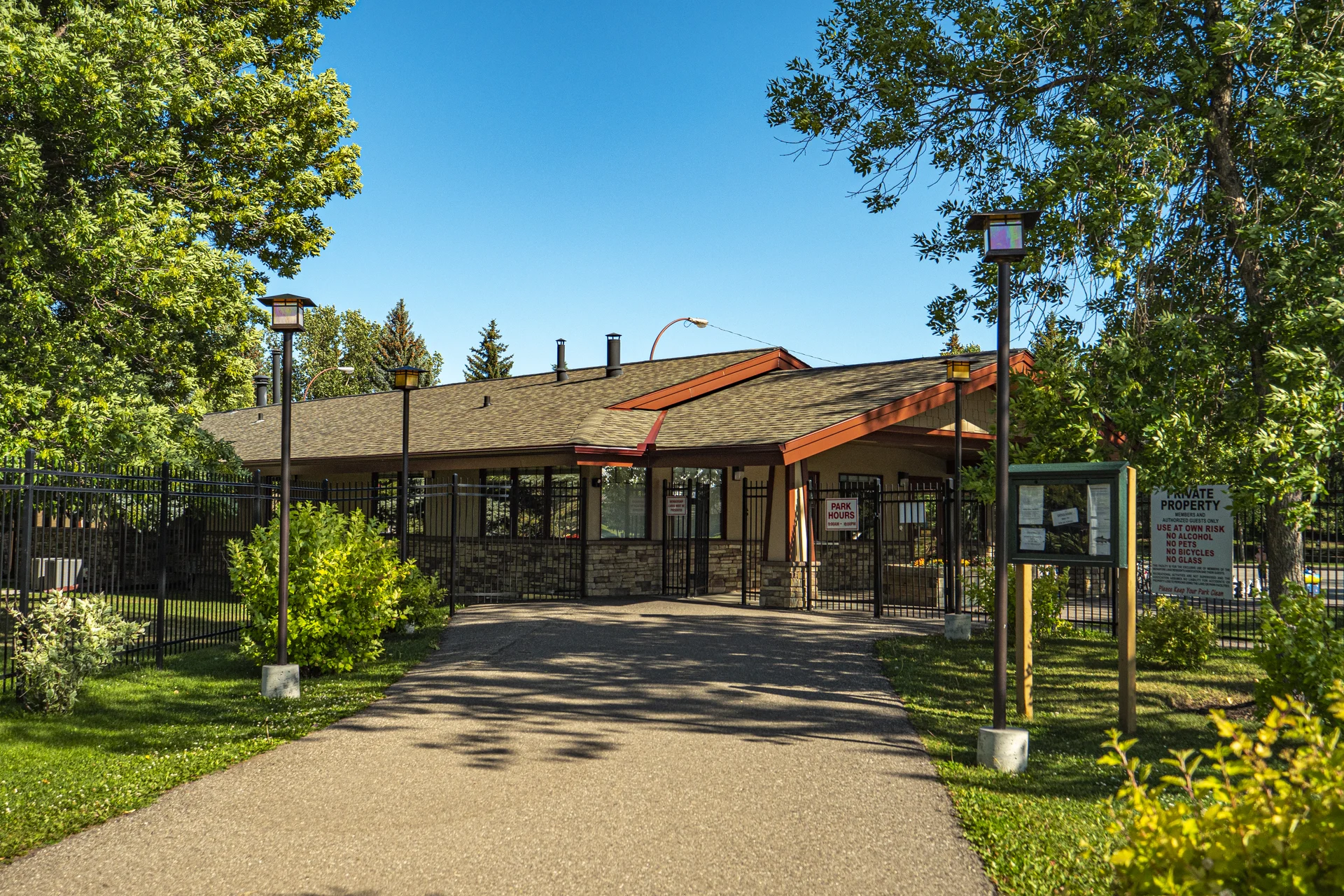 Midnapore lake-park entrance building behind black metal gates, with lantern posts, mature trees and a paved approach